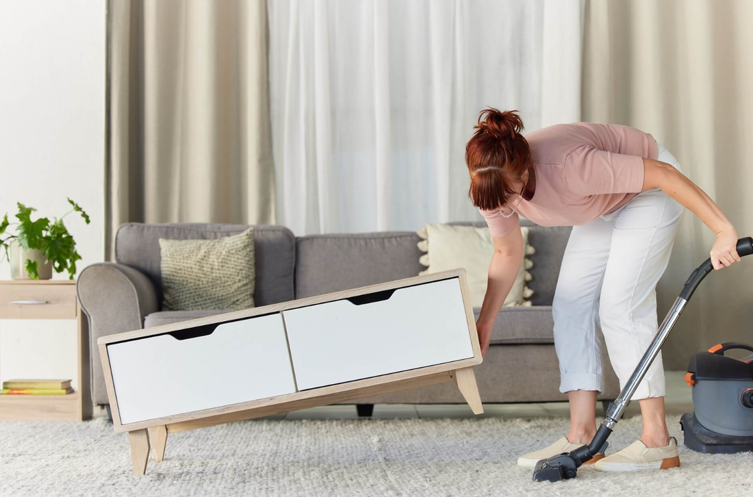 A person vacuuming under a cabinet