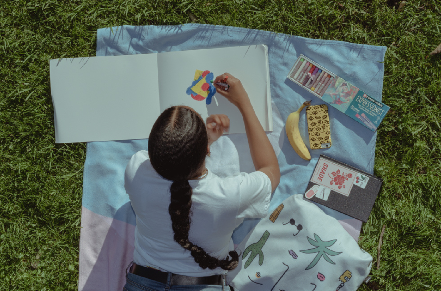 Rewina Beshue laying in a sunny park doing artwork