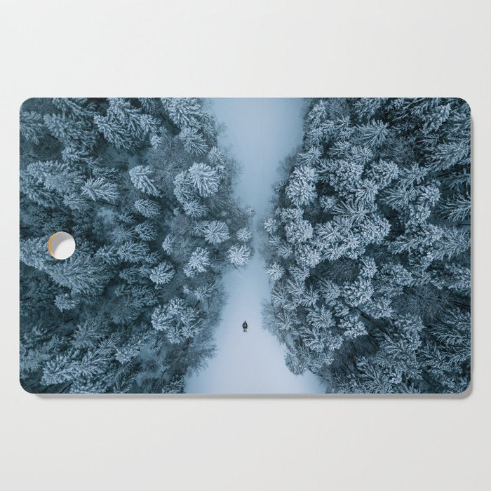 Man lying in the snow on a frozen lake in a winter forest - Landscape Photography Cutting Board Gallery Image 1